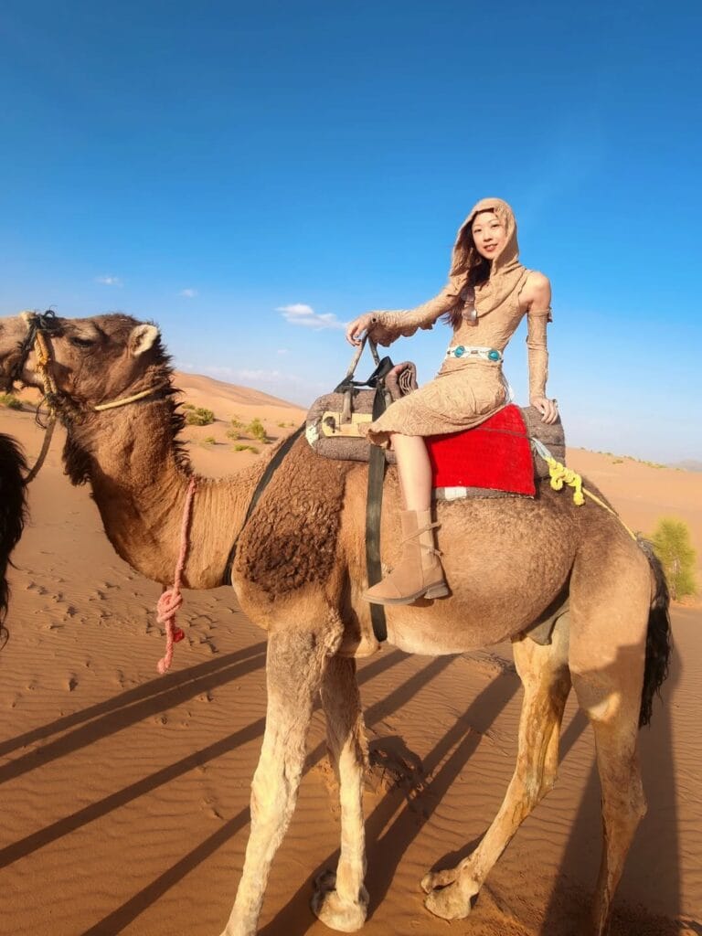 Solo woman riding a camel through the Sahara dunes in Merzouga, Morocco